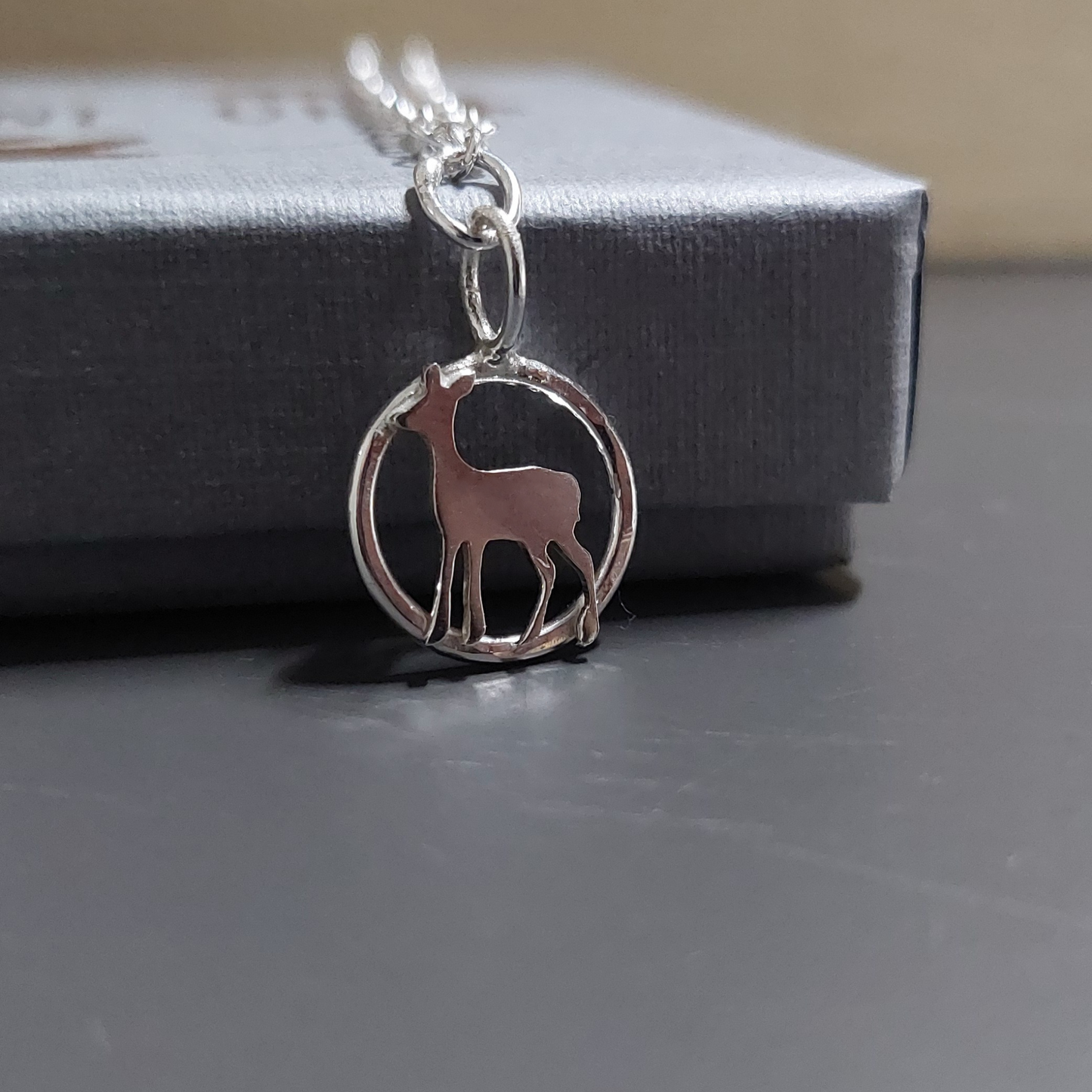Silver necklace with a deer charm on a gift box