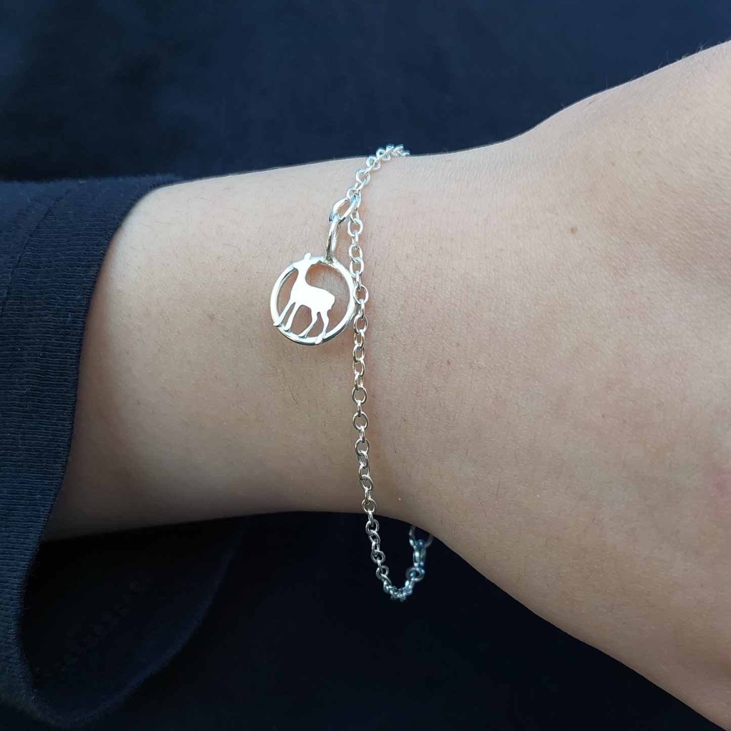 Silver bracelet with a deer charm on a wrist against a dark background