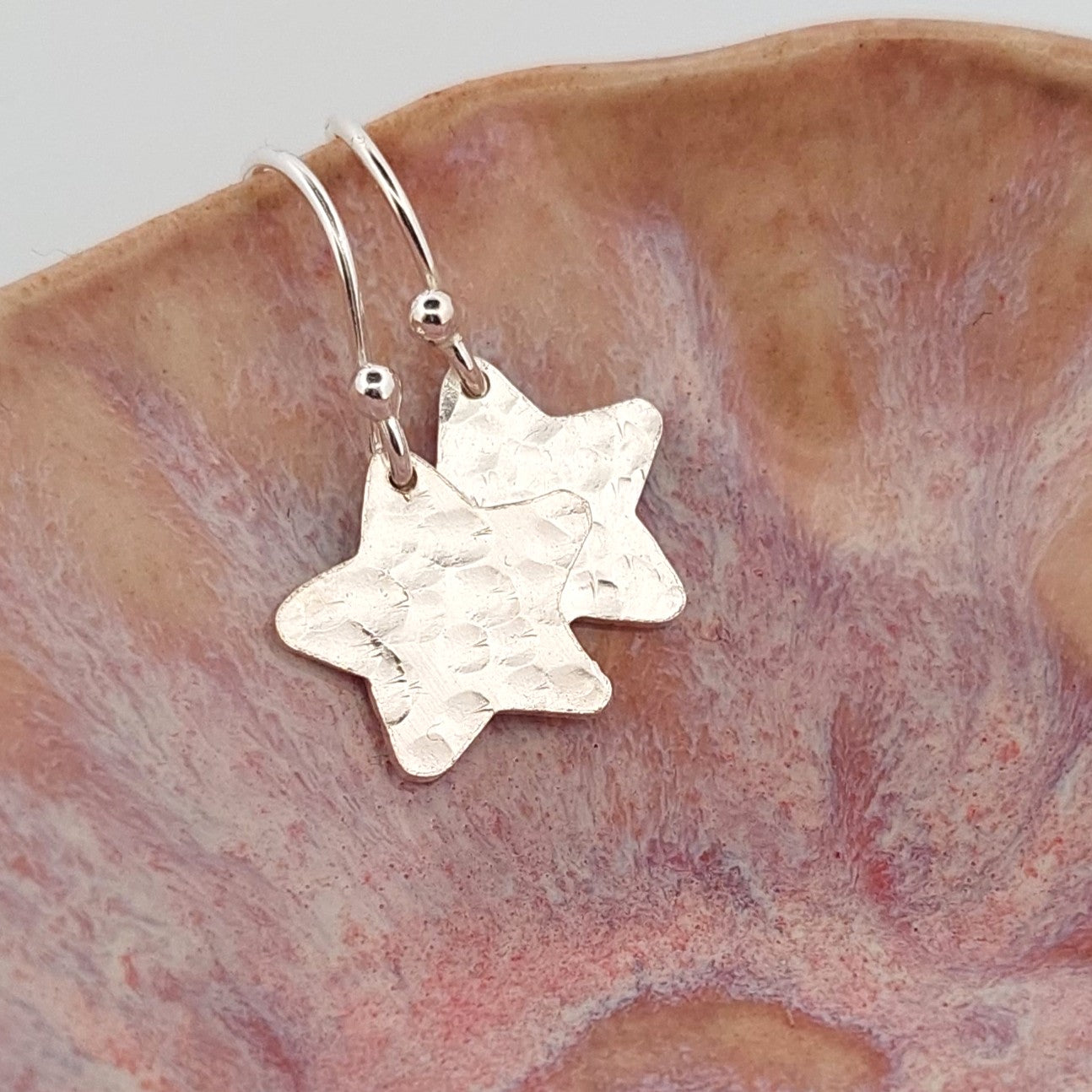 Silver star-shaped earrings on a textured brown surface