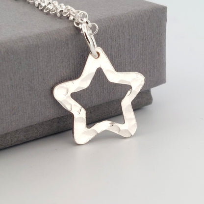 Silver star-shaped pendant on a chain against a gray background