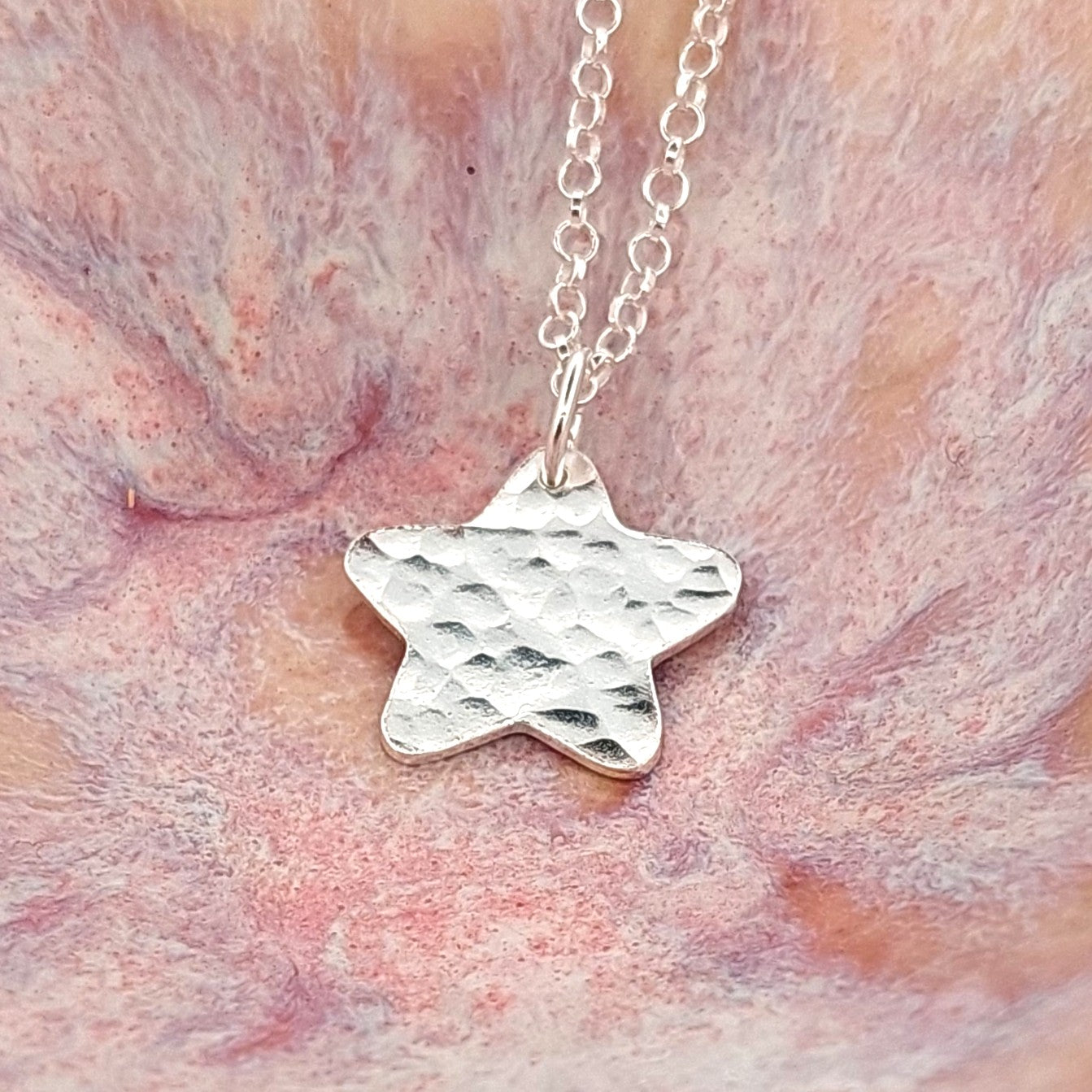 Silver star-shaped pendant on a chain against a pink and orange marbled background