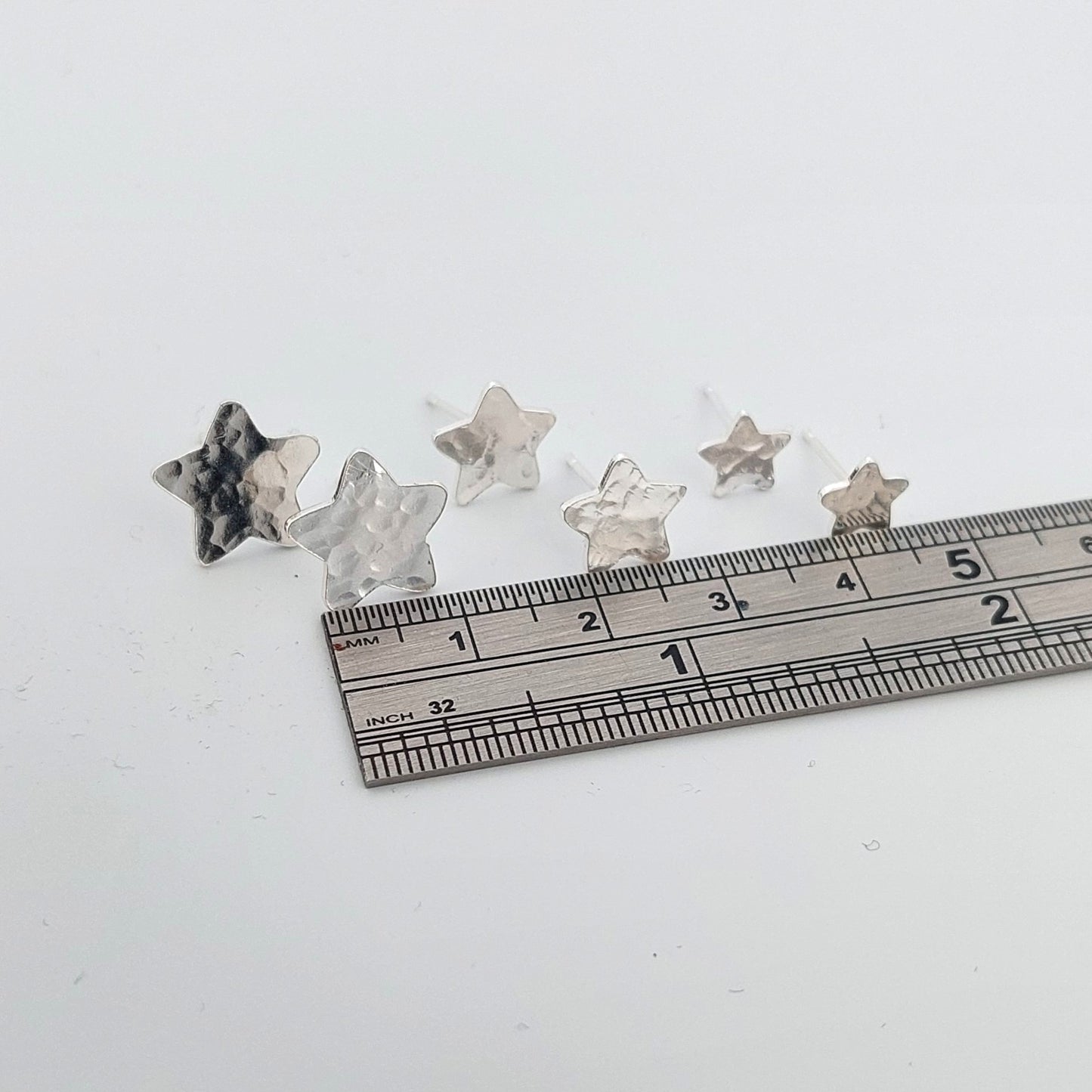 Three sizes of Star-shaped stud earrings with a ruler for scale on a white background