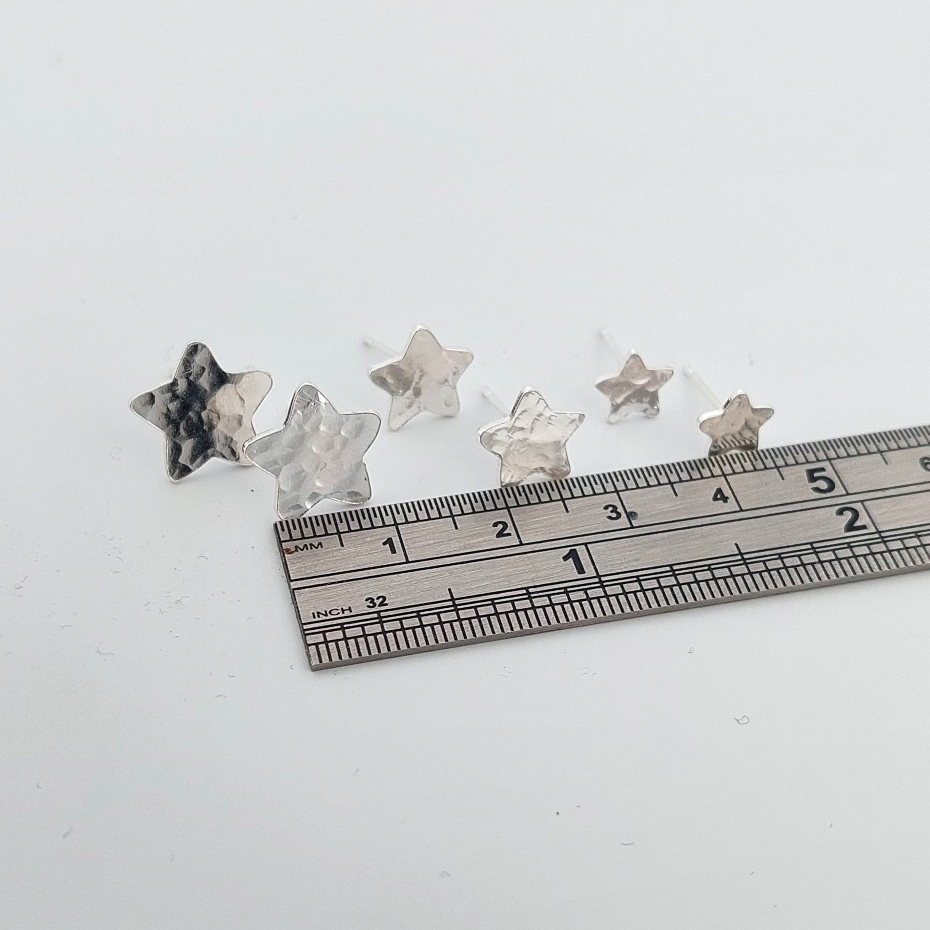 Three sizes of Star-shaped stud earrings with a ruler for scale on a white background