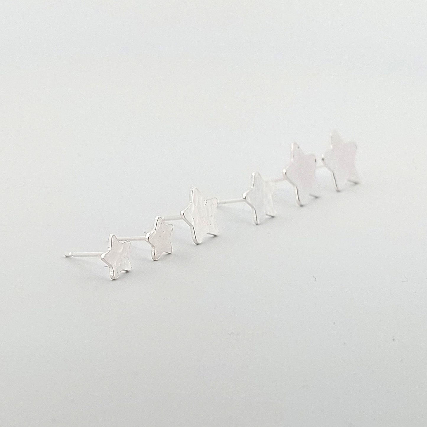 Three sizes of Silver star-shaped earrings on a light gray background