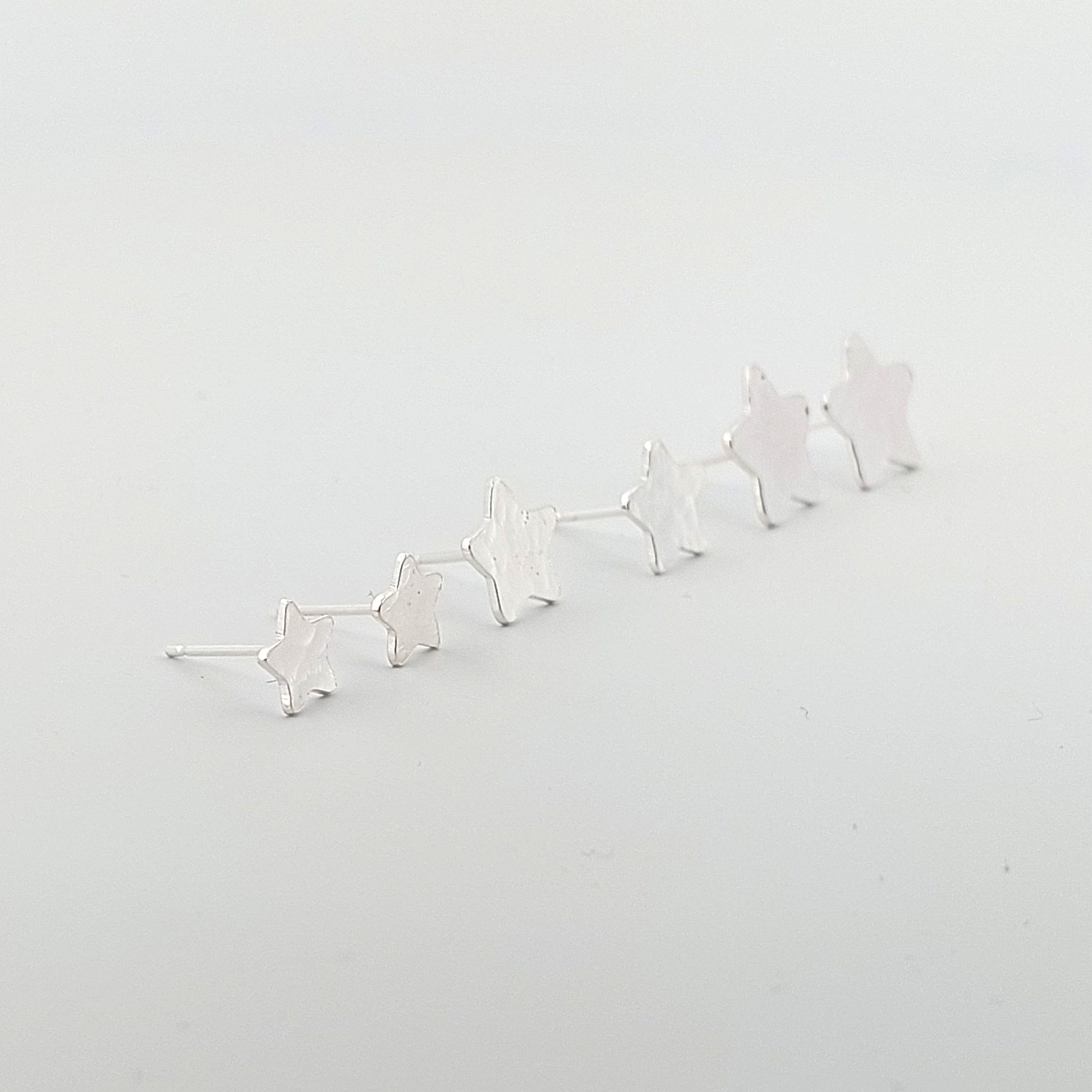 Three sizes of Silver star-shaped earrings on a light gray background